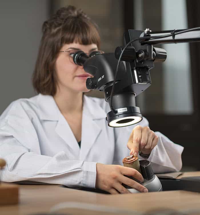 Female scientist examining a timepiece through a microscope in a laboratory setting.