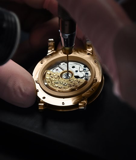 Intricate gold timepiece movement being assembled with precision tools.