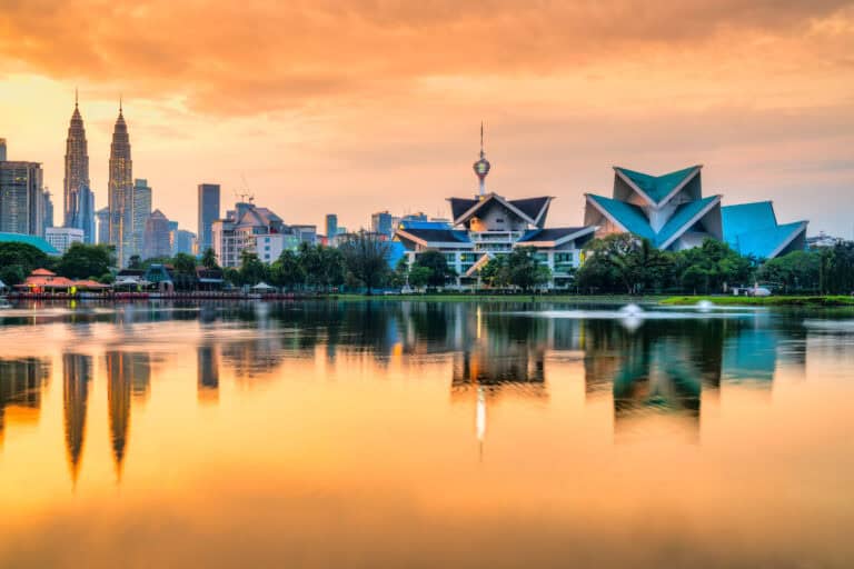 A stunning cityscape featuring iconic architecture reflected on a calm body of water at sunset.