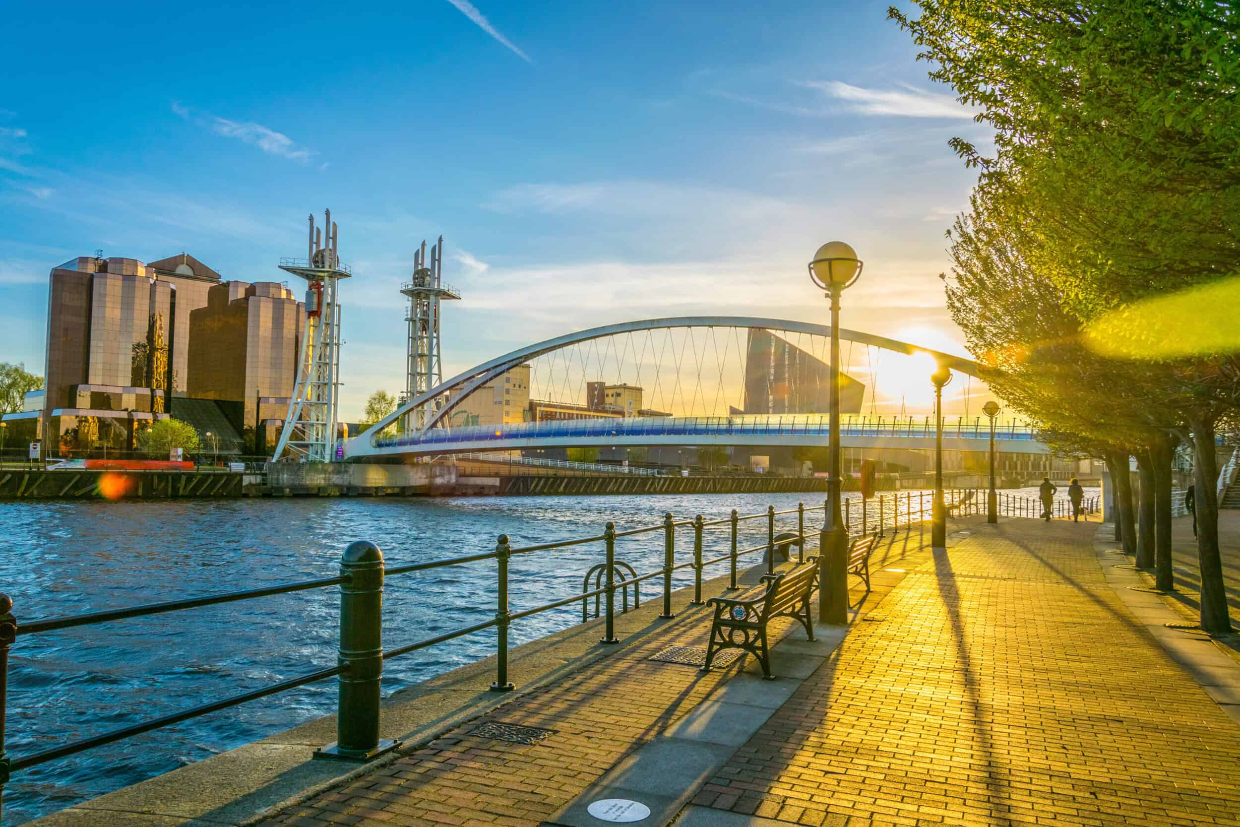 Scenic riverside view with modern bridge and city skyline at sunset.