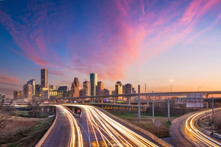 Modern city skyline with vibrant sunset and dynamic light trails on highways.