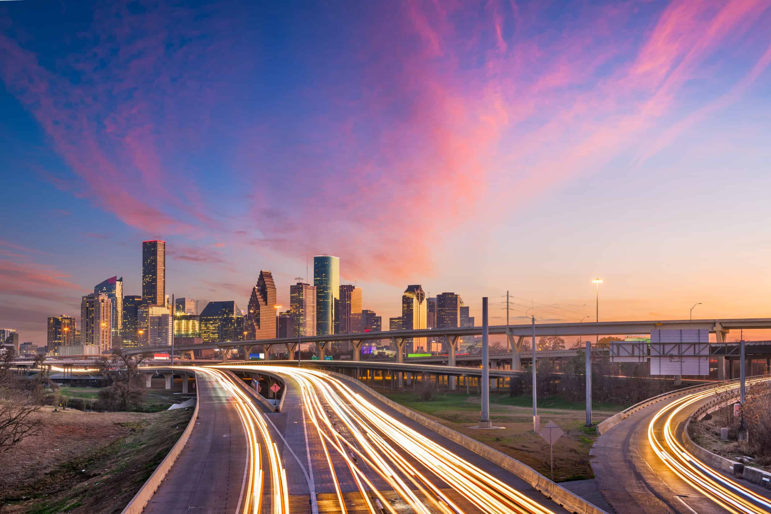 Modern city skyline with vibrant sunset and dynamic light trails on highways.