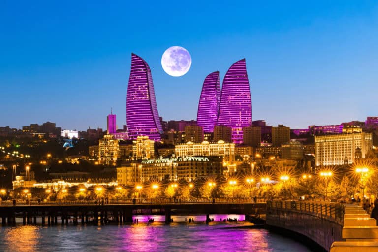 A stunning cityscape of Baku illuminated at night with modern skyscrapers and a full moon in the sky.