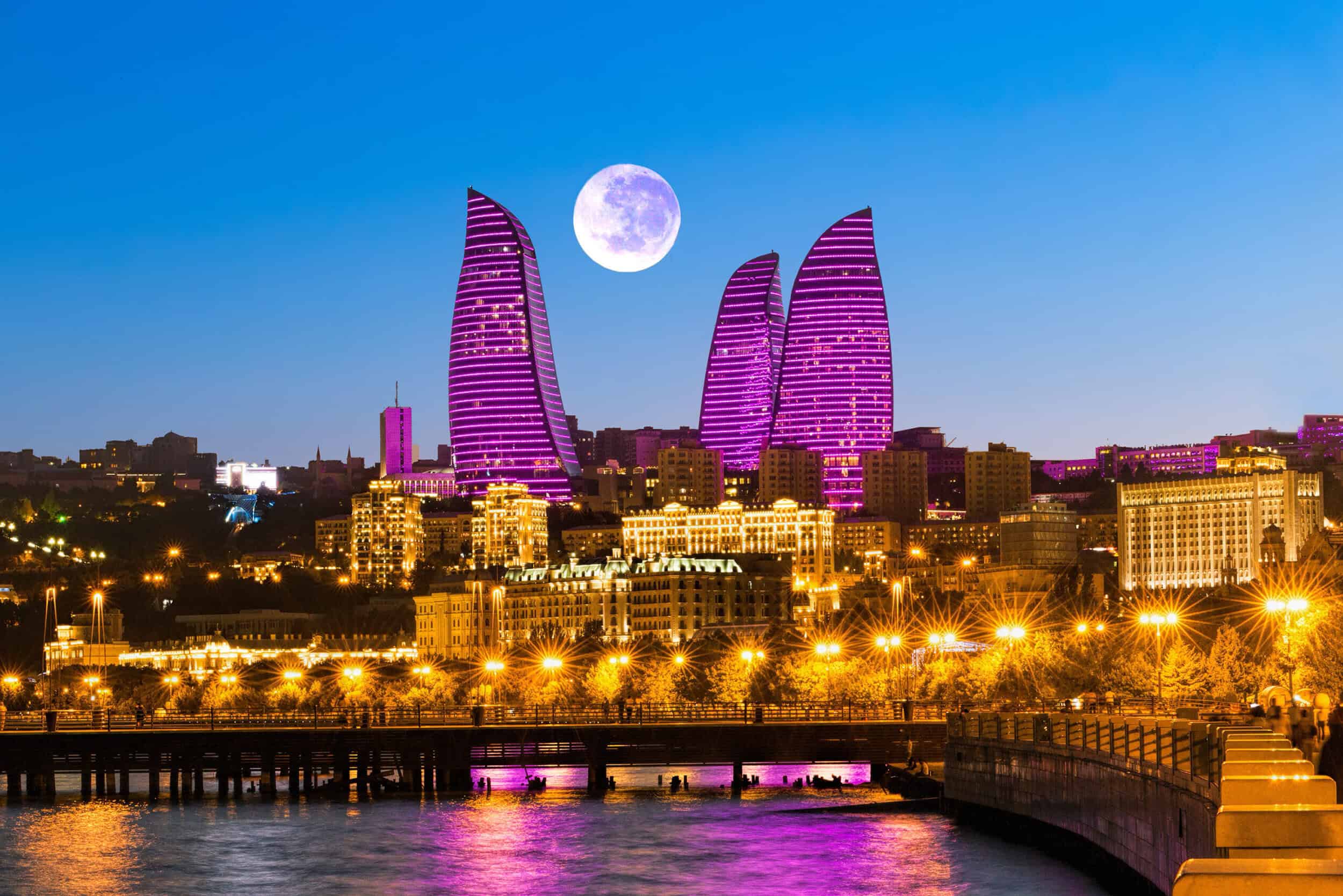 A stunning cityscape of Baku illuminated at night with modern skyscrapers and a full moon in the sky.