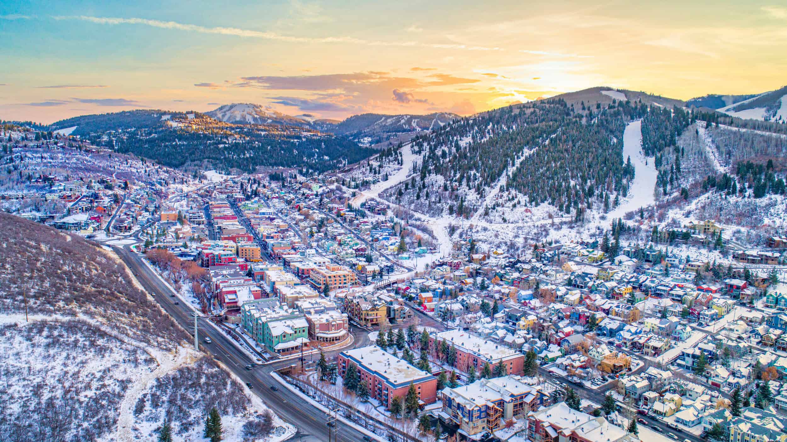 Scenic winter mountain town with colorful buildings and snow-covered slopes at sunset.