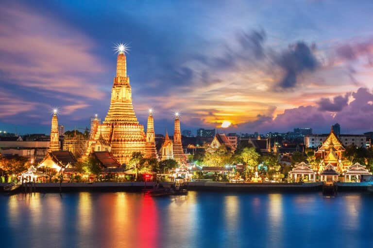Elegant Thai temple illuminated at sunset with vibrant sky reflections on the river.