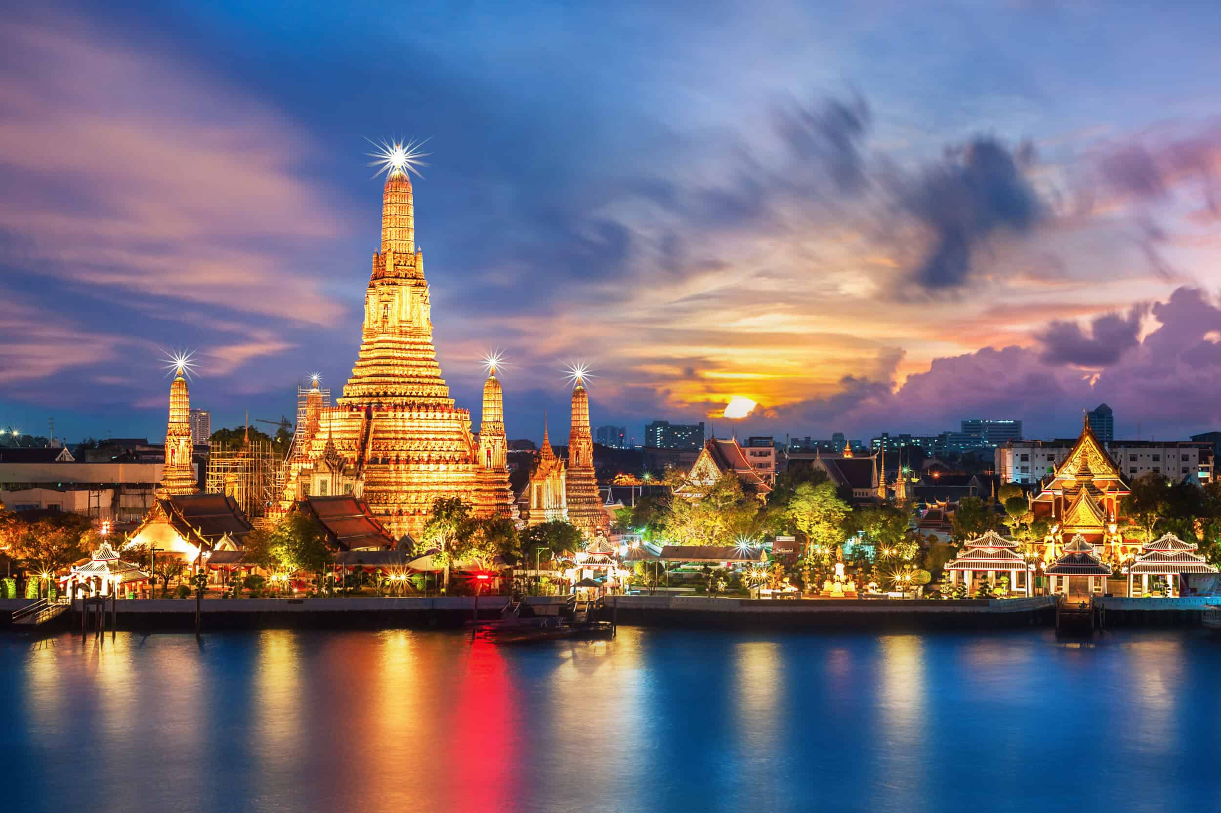 Elegant Thai temple illuminated at sunset with vibrant sky reflections on the river.