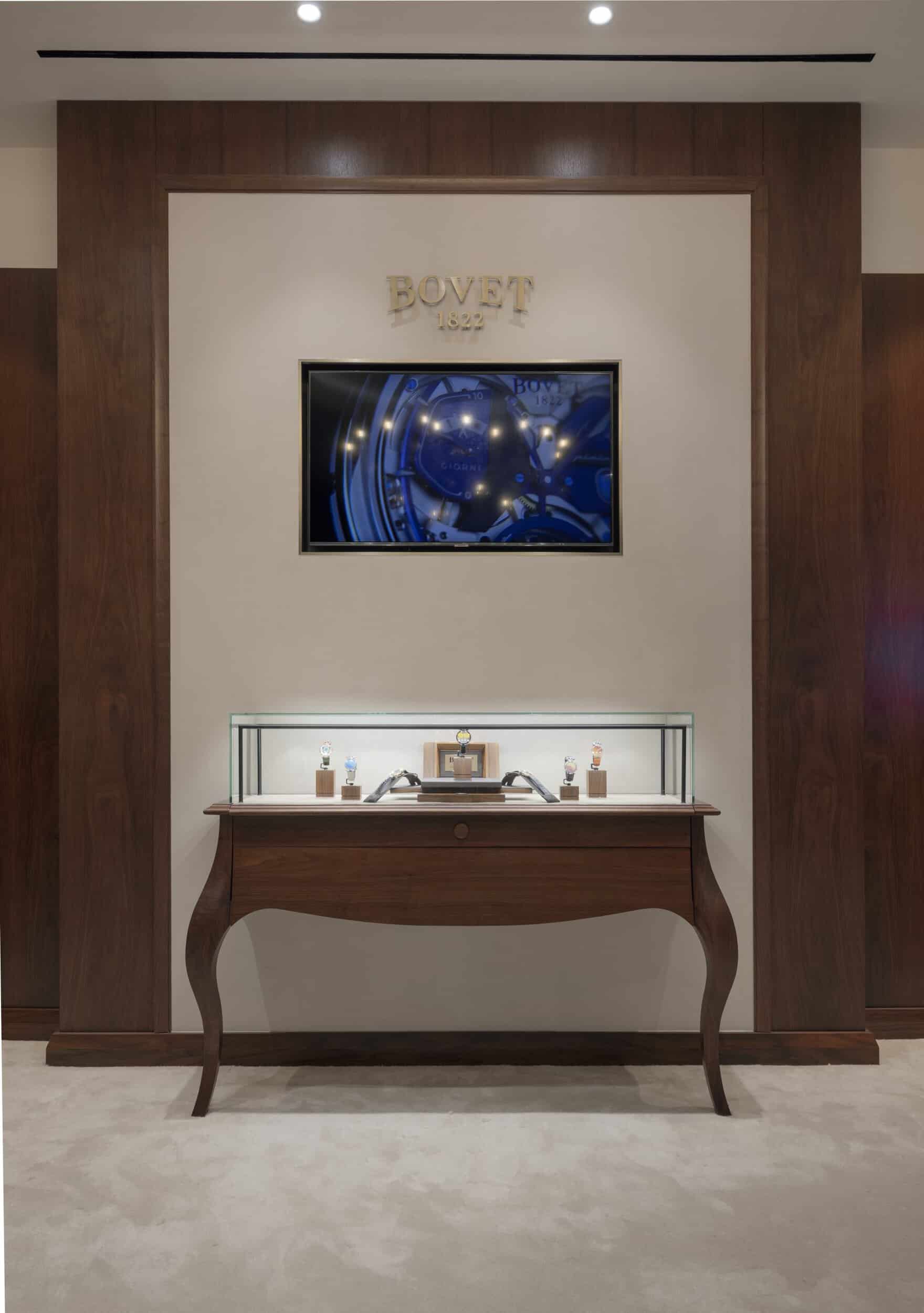 Elegant Bovet display with a digital clock and luxury timepieces showcased on a classic wooden table.