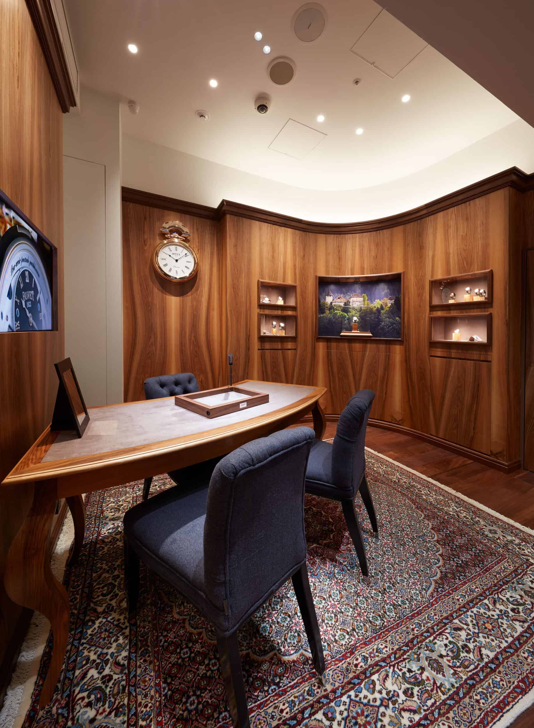 Elegant wooden-paneled conference room with a classic clock, plush chairs, and a large screen displa.