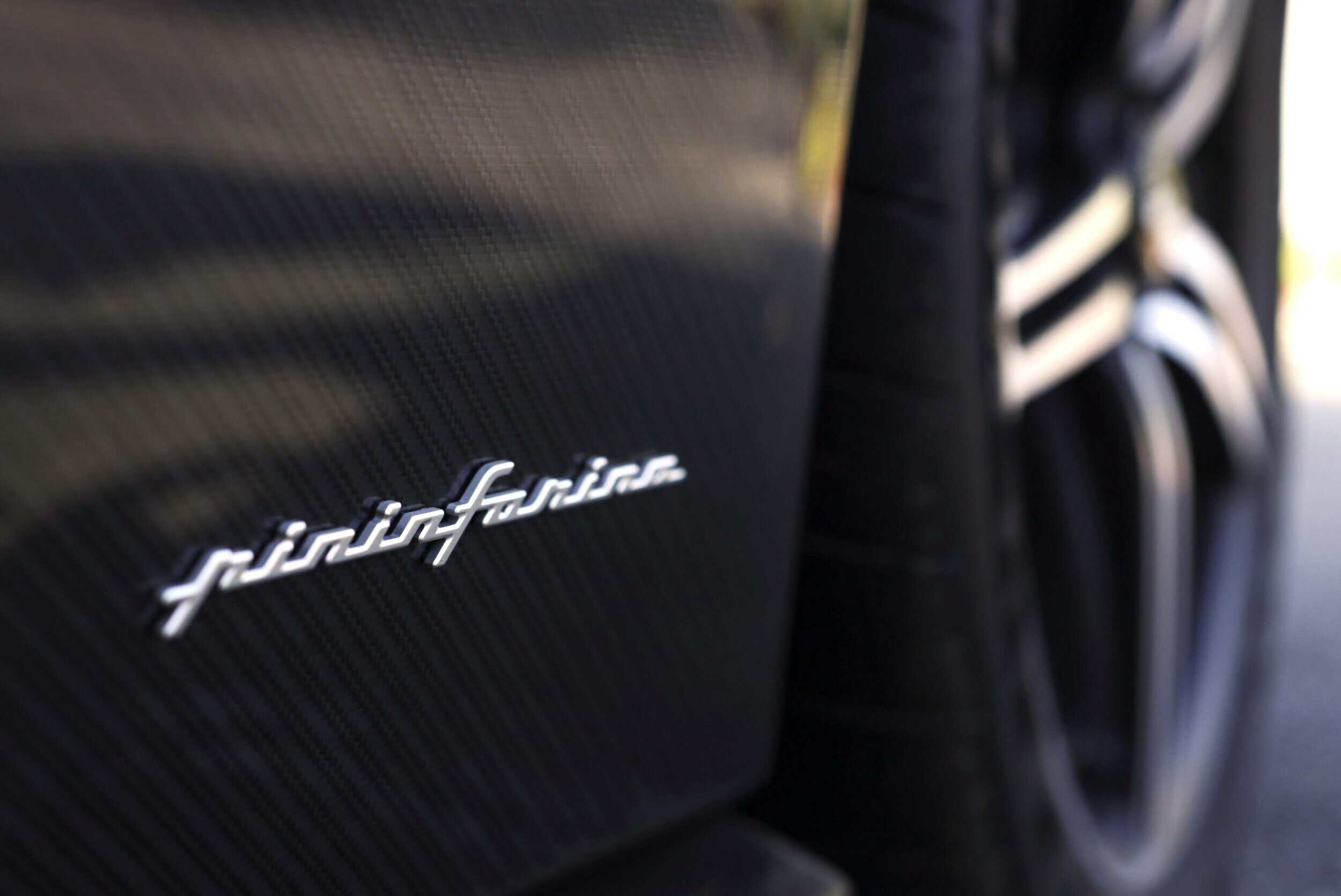 Close-up of a Pininfarina logo on a luxury vehicle's carbon fiber surface.