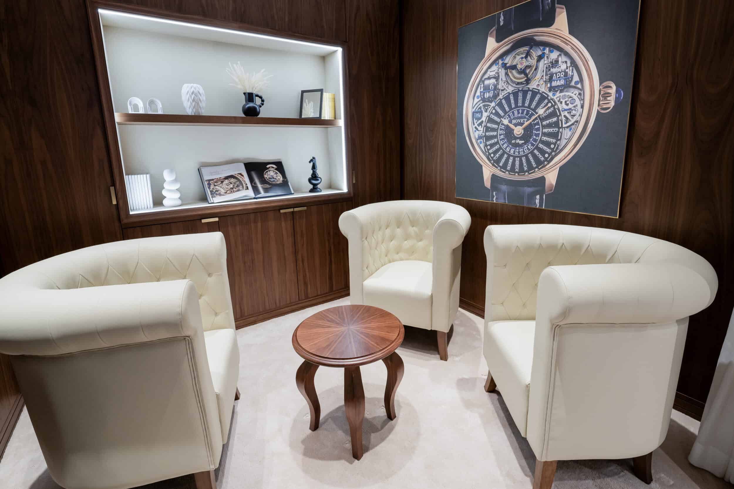 Elegant seating area with cream armchairs and a wooden table, showcasing luxury timepieces in a soph.