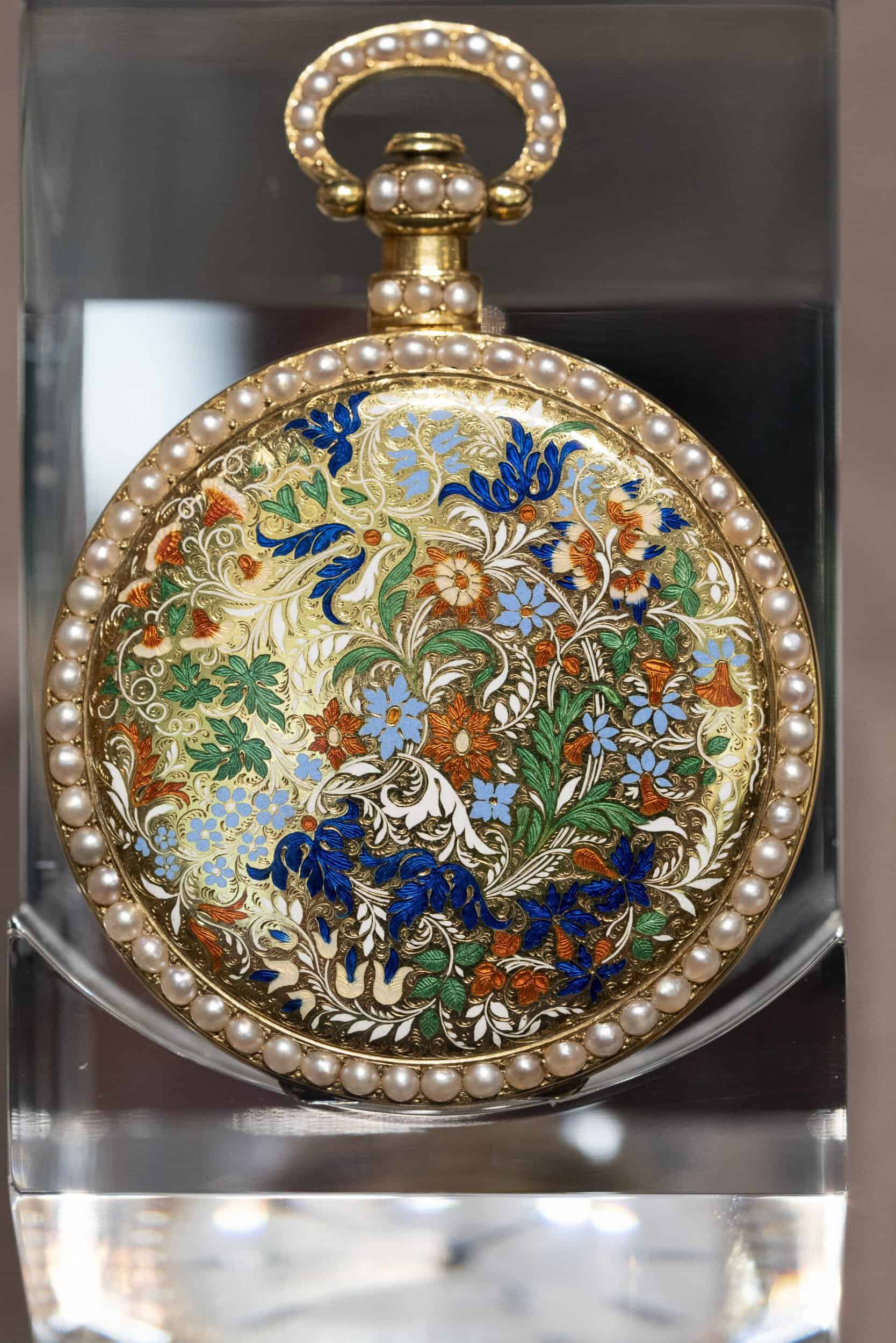 Ornate antique pocket timepiece with pearl accents and intricate floral design.