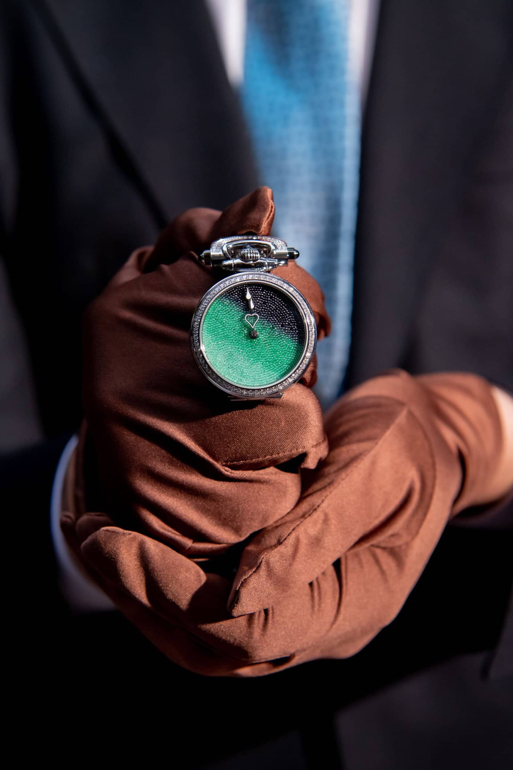 Elegant green dial timepiece held by a person in formal attire and brown gloves.