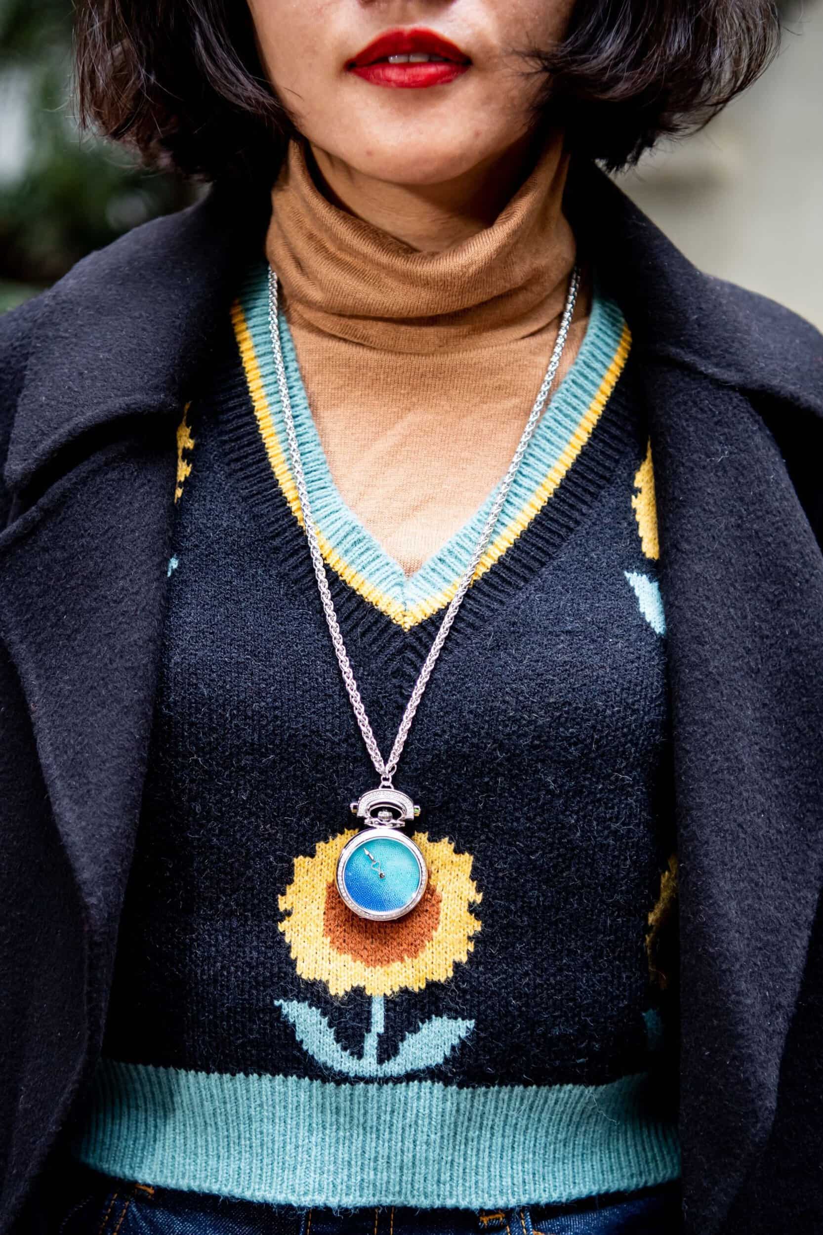 Elegant woman wearing a vibrant sweater and a striking blue timepiece pendant necklace.