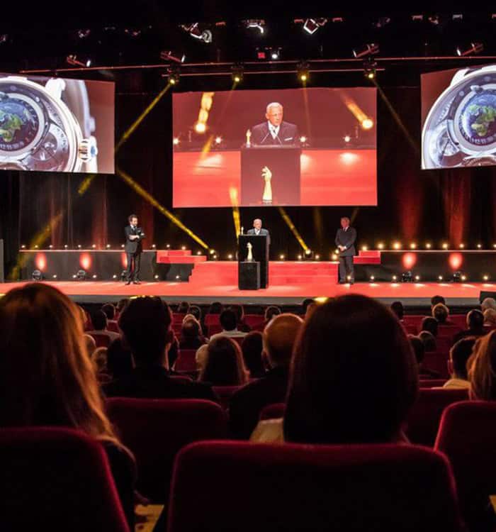 Elegant Bovet timepiece showcased at a formal event with a stage and large screens.